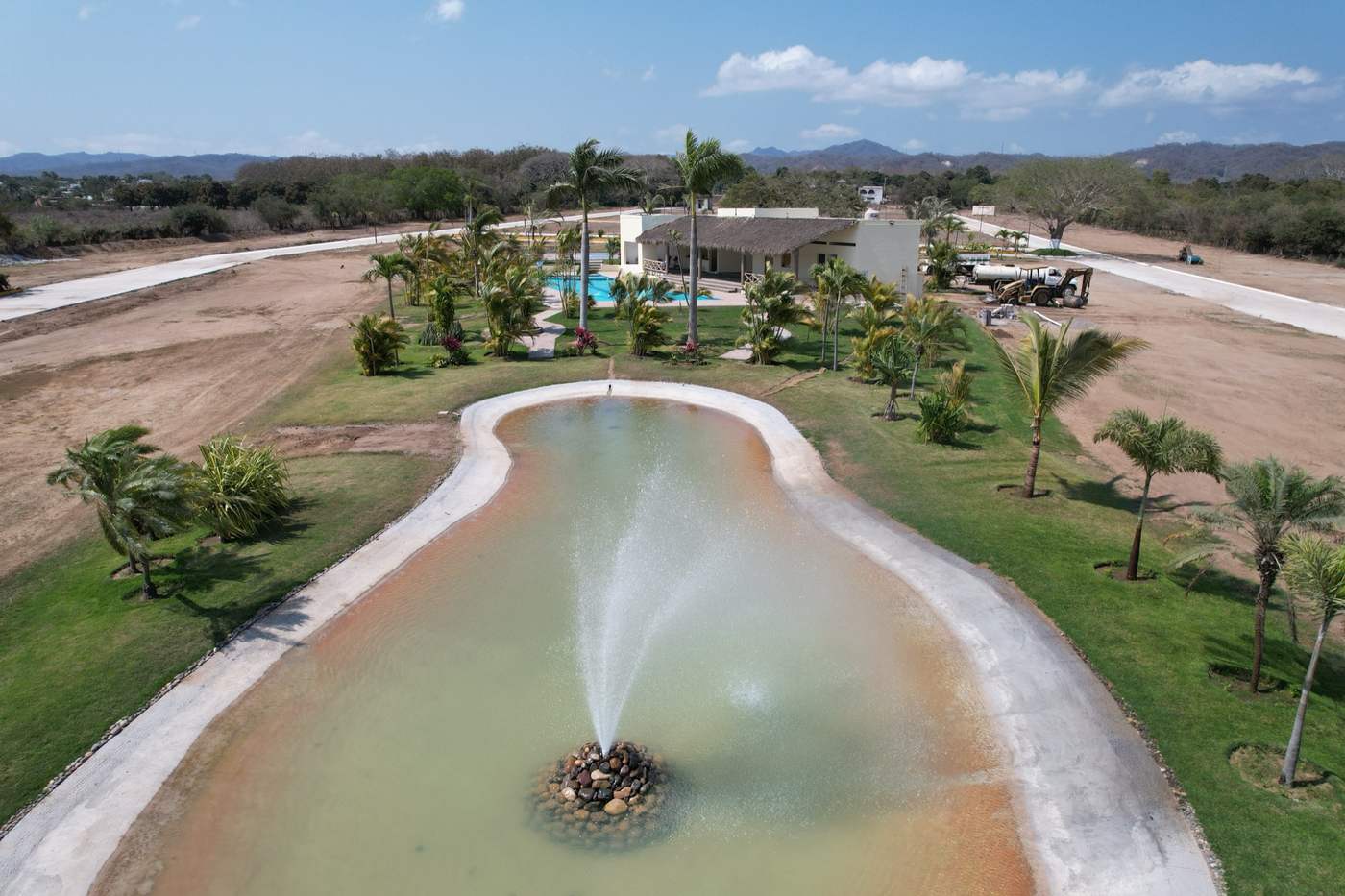 Lago con fuente y palmeras, con la casa club al fondo